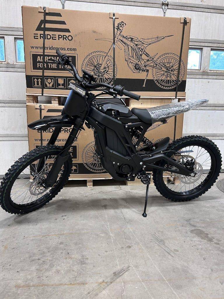 Black E-Ride Pro electric dirt bike in front of packaging box in a garage